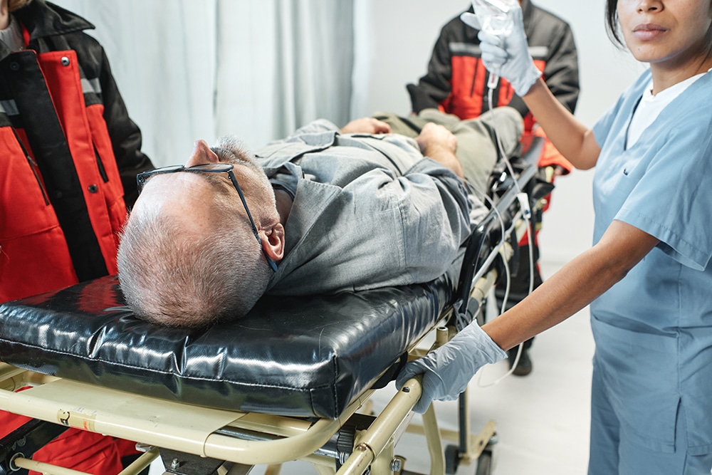 Horizontal shot of ambulance and emergency department workers bringing mature patient with heart attack on stretcher into hospital